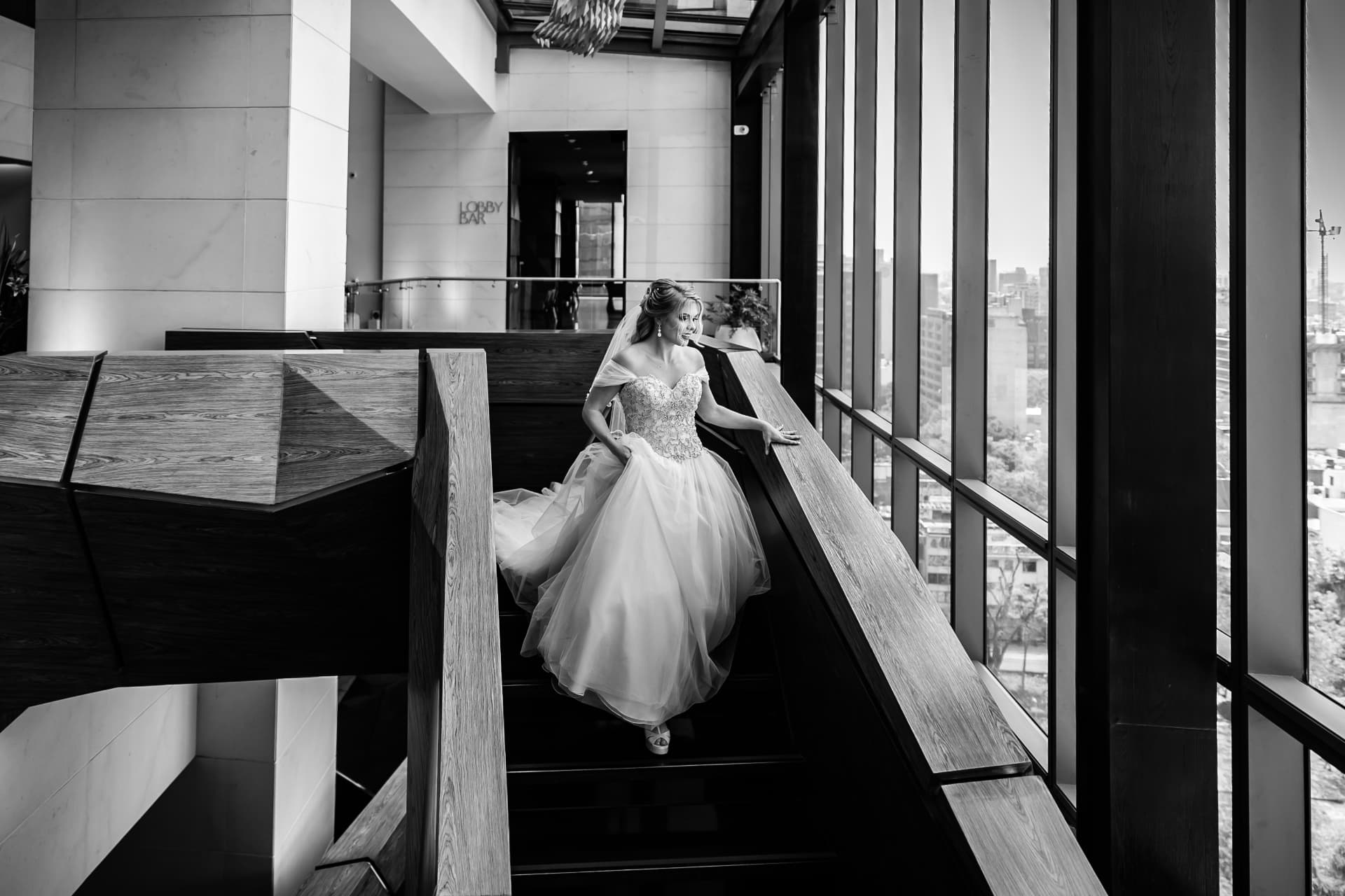 Novia descendiendo una escalera moderna durante los preparativos, fotografía en blanco y negro