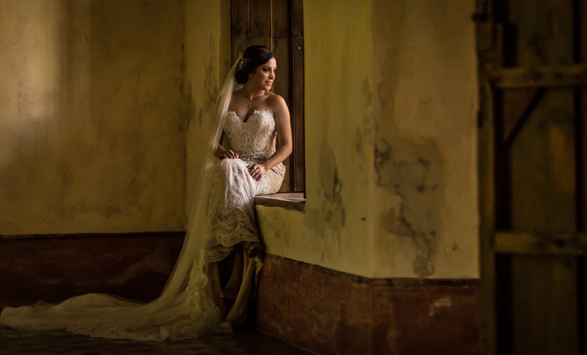 Novia sentada junto a una ventana en un interior histórico con luz cálida