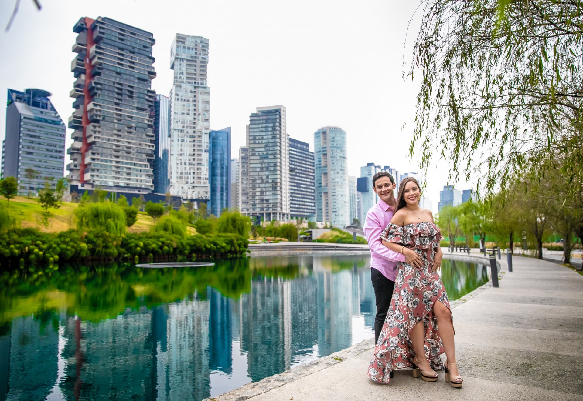 Pareja abrazada junto a un lago urbano y arquitectura contemporánea, sesión save the date