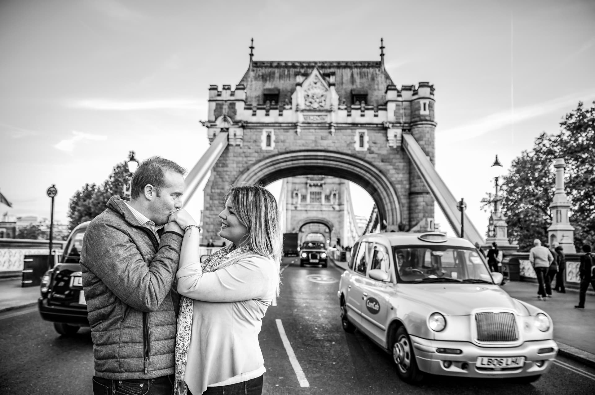 Pareja frente al Tower Bridge con un taxi londinense, sesión save the date en blanco y negro