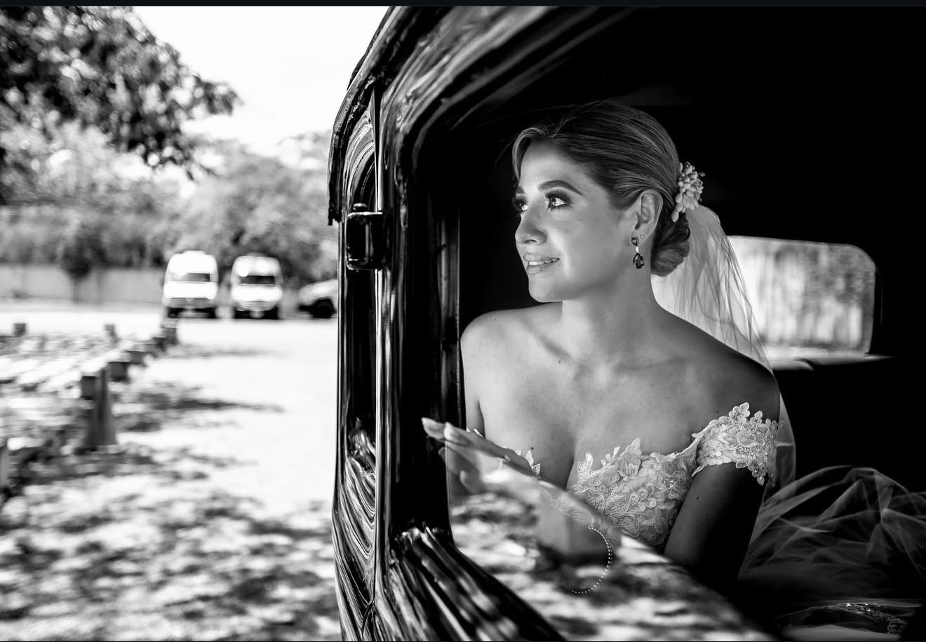 Novia sonriendo desde un auto clásico, fotografía de boda en blanco y negro