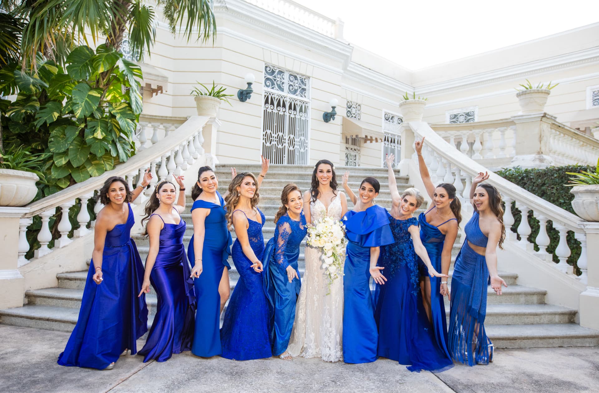 Novia celebrando con sus damas vestidas de azul frente a una escalinata
